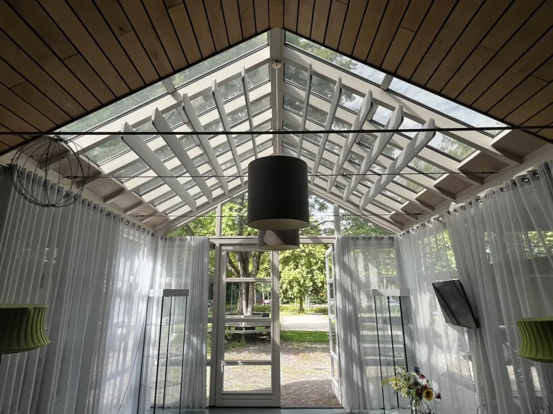 Ontvangstruimte van Dorpshuis De Groeneberg met houten balken, grote glaspartijen en tien lichtgrijze EASYfelt baffles die de akoestiek verbeteren.